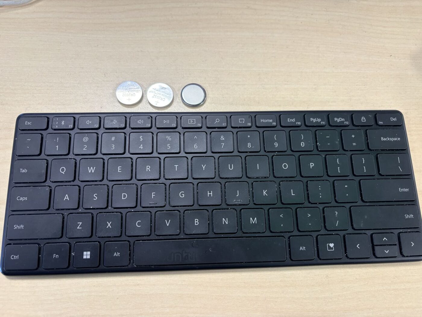 Bluetooth keyboard with three CR2032 coin cells removed from the bay resting above it, two positive-side up and one negative-side up